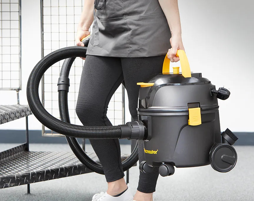 Cleaner carrying Vacmaster Vacuum Cleaner across office